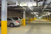 Indoor parking garage with concrete pillars painted yellow at the bottom, several parked cars, and overhead lighting fixtures.