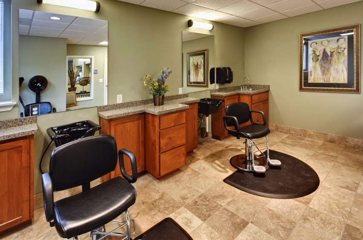 Interior salon/hair-styling room with two barber chairs, shampoo sinks, mirrors, granite counters and wooden cabinetry.