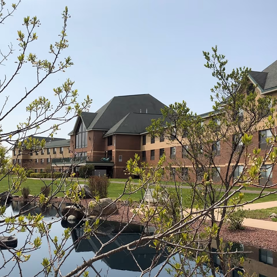 Multi-story brick senior living building with a pond and budding trees in the foreground.