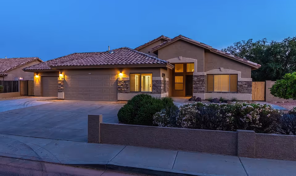 Single-story assisted living home exterior at dusk with illuminated entrance and two garage bays.