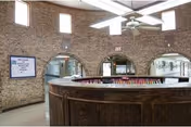 Circular wooden reception desk in a round brick-walled interior with arched doorways and a ceiling fan.