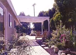 An exterior walkway through a landscaped courtyard leads to a covered seating area at Casa Naomi.