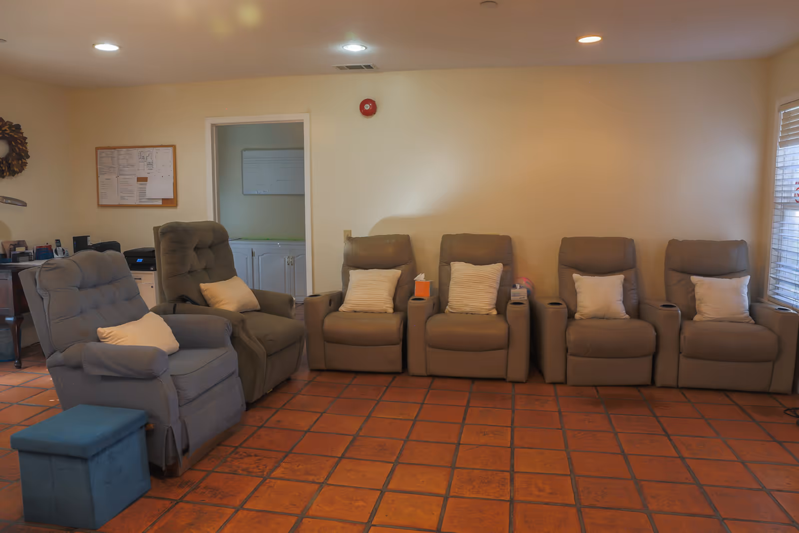 A lounge with a row of recliner chairs and pillows on a tiled floor in a senior living facility.