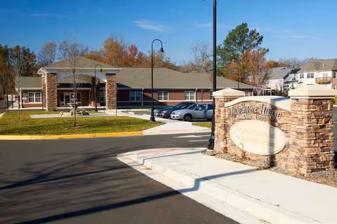 Exterior view of The W Assisted Living entrance with a stone sign and parked cars.