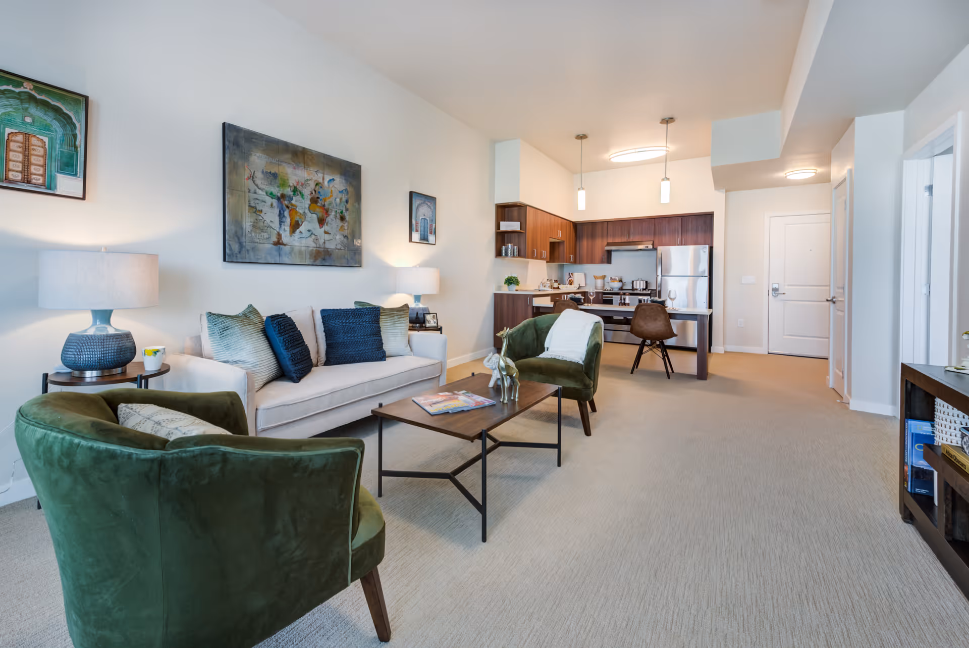 Bright open living room with a sofa, green armchairs, coffee table and an open kitchen in the background.