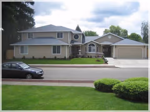 Two-story beige senior care building with a driveway, lawn, and a parked car.