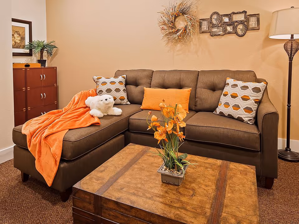 Cozy living room with a brown sectional sofa dressed with orange pillows and throw, a wooden coffee table with a floral arrangement, and a standing lamp.