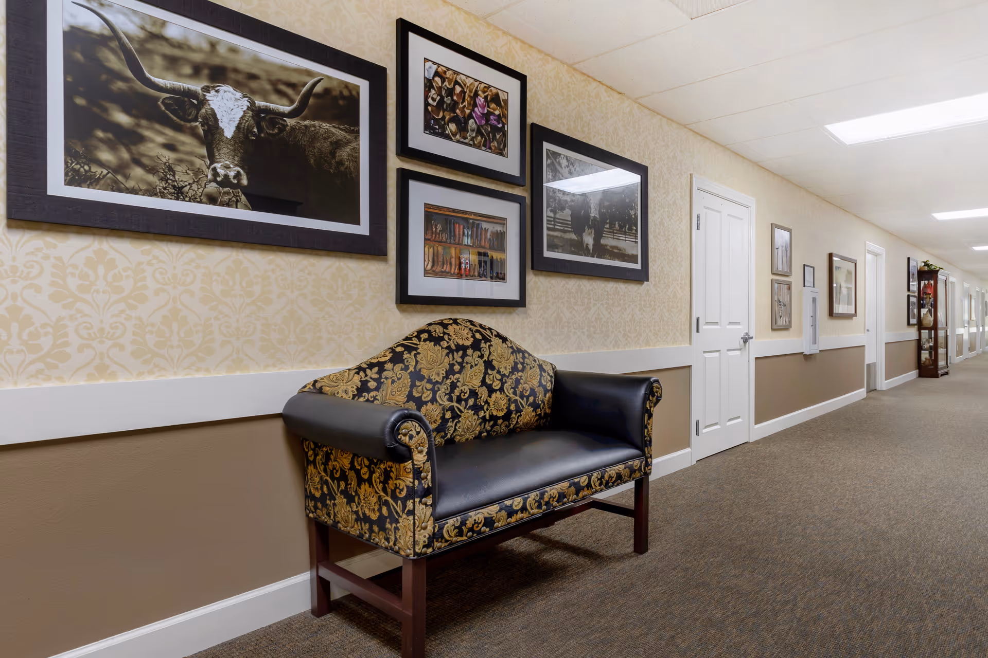 Carpeted interior hallway with a patterned upholstered bench and framed artwork along the walls.