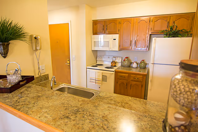 Small kitchen with a laminate countertop breakfast bar, stainless sink, white stove and refrigerator, and wooden cabinets.