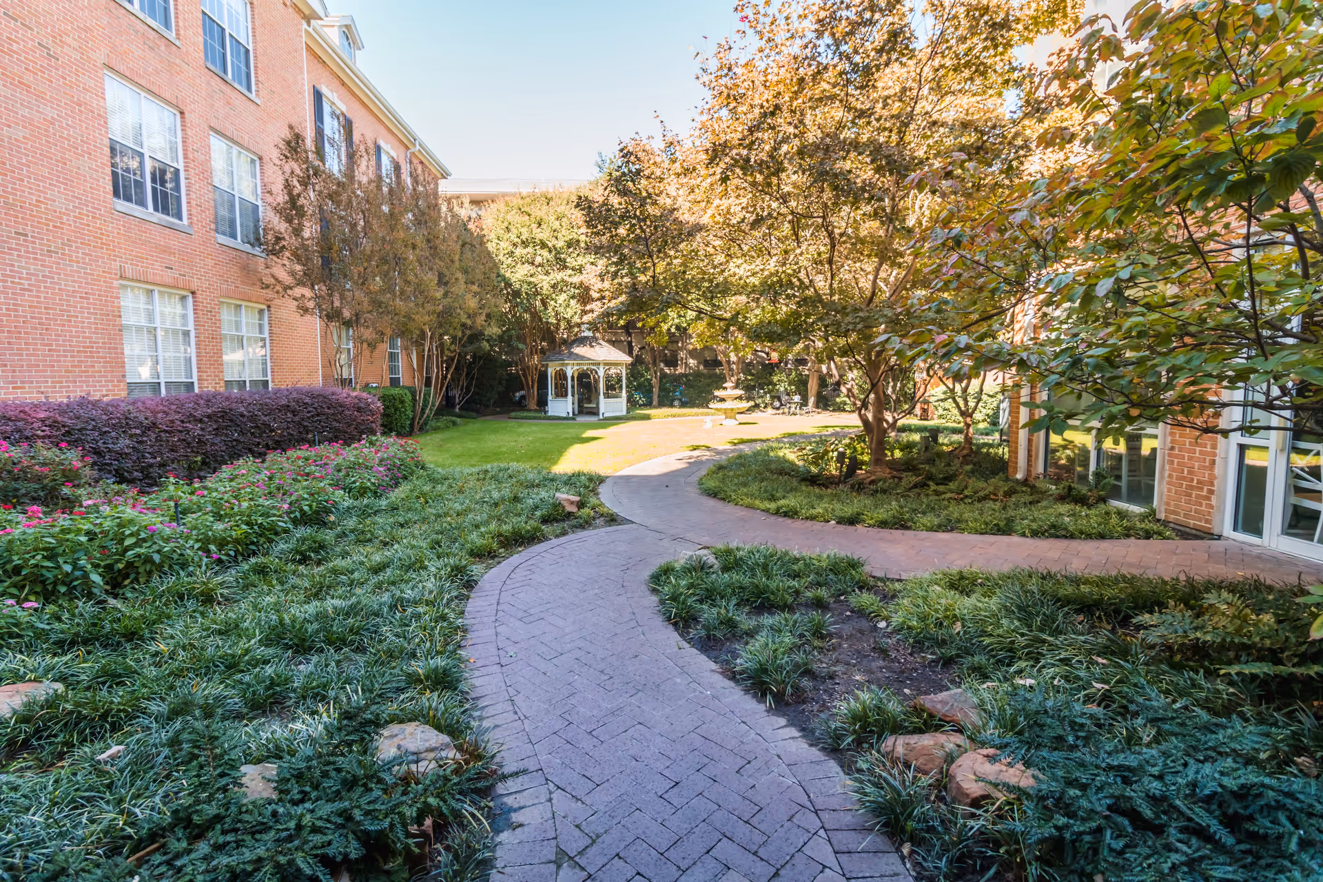 A landscaped garden pathway surrounded by greenery and flowers at Caruth Haven Court, featuring a gazebo in the background.