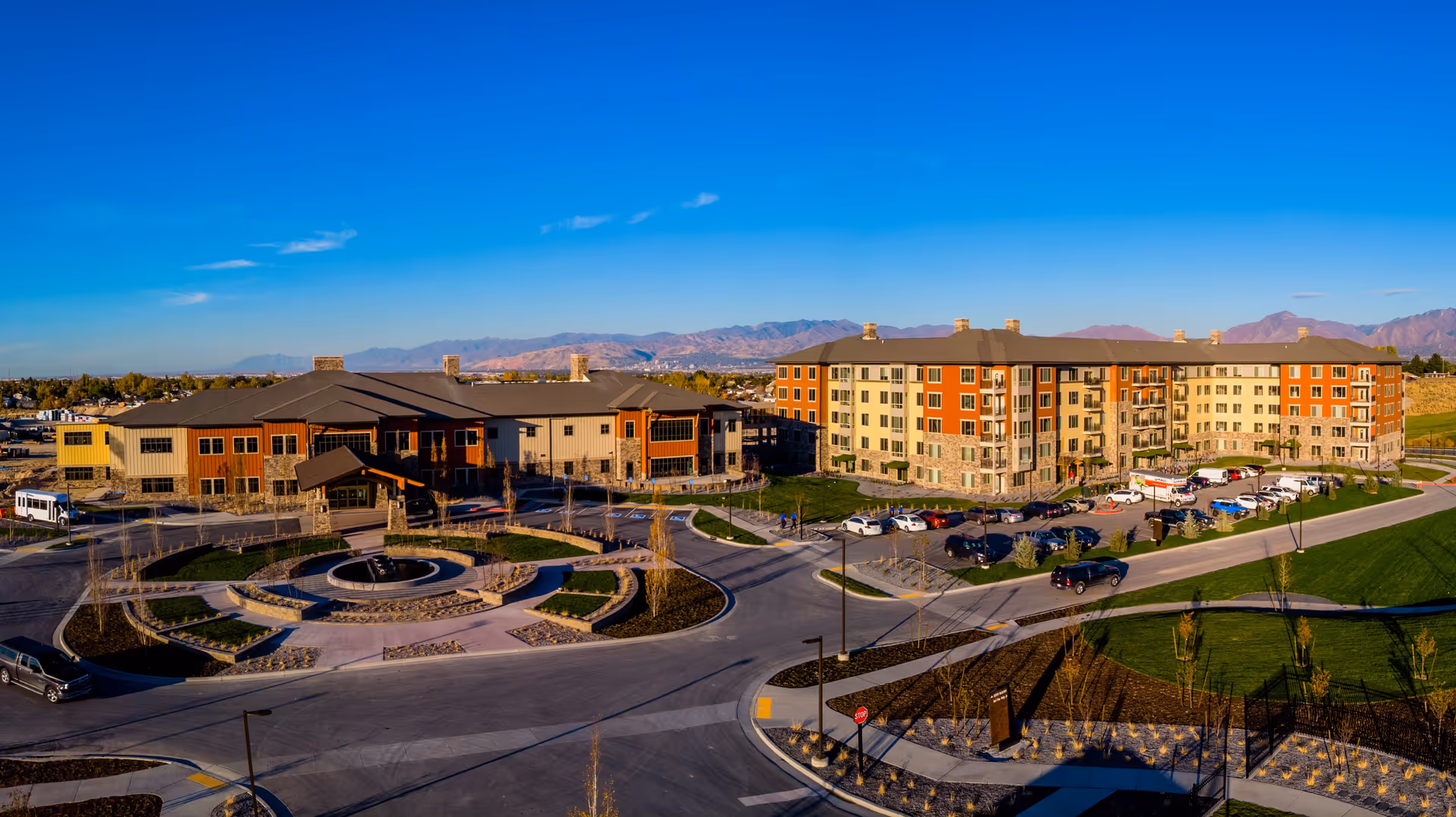 Aerial view of the Summit Vista senior living complex with multi-story buildings, a circular driveway, landscaped grounds, and mountains in the background.