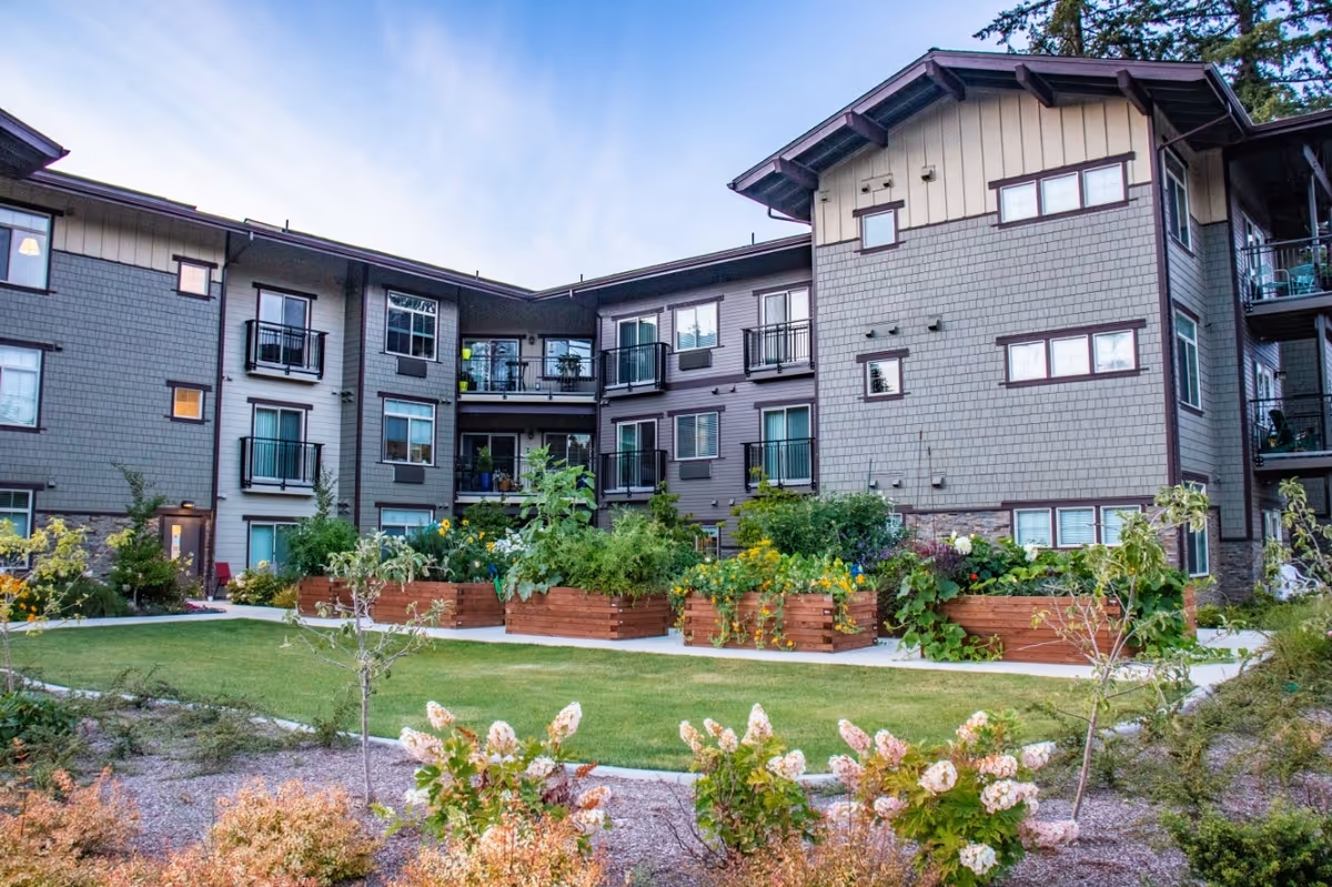 Three-story memory care building exterior with balconies, a grassy courtyard and wooden raised garden beds.
