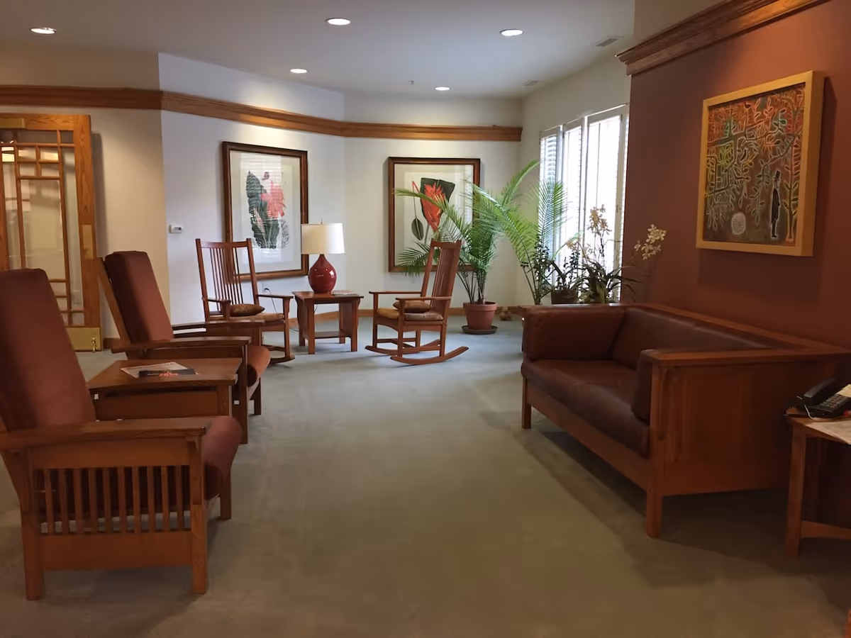 A comfortable sitting area with wooden armchairs, a leather sofa, side tables, potted plants and framed artwork.