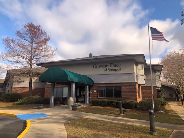Front entrance of Crowne Place of Springhill, a two-story brick building with a green awning and an American flag.
