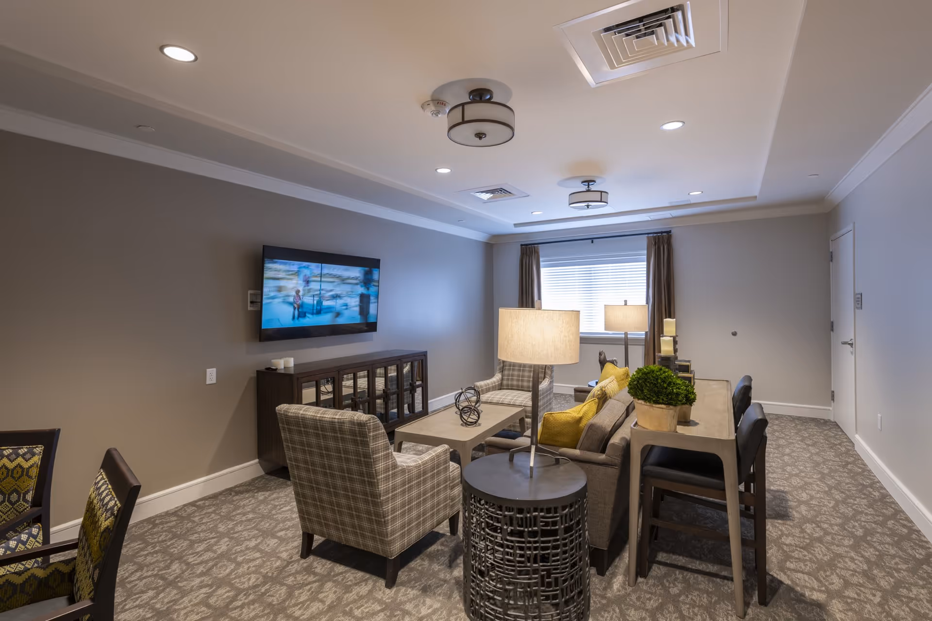 Comfortable communal living room with a sofa, armchairs, wall-mounted TV, lamps, and a console table.