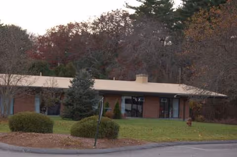 Single-story brick facility with a flat roof, curved driveway, and manicured lawn in front.