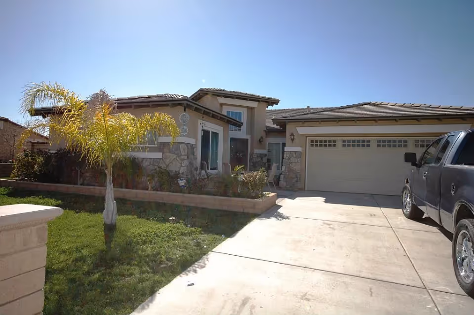 Front view of a single-story house with an attached garage, driveway, and small front yard with a palm tree.