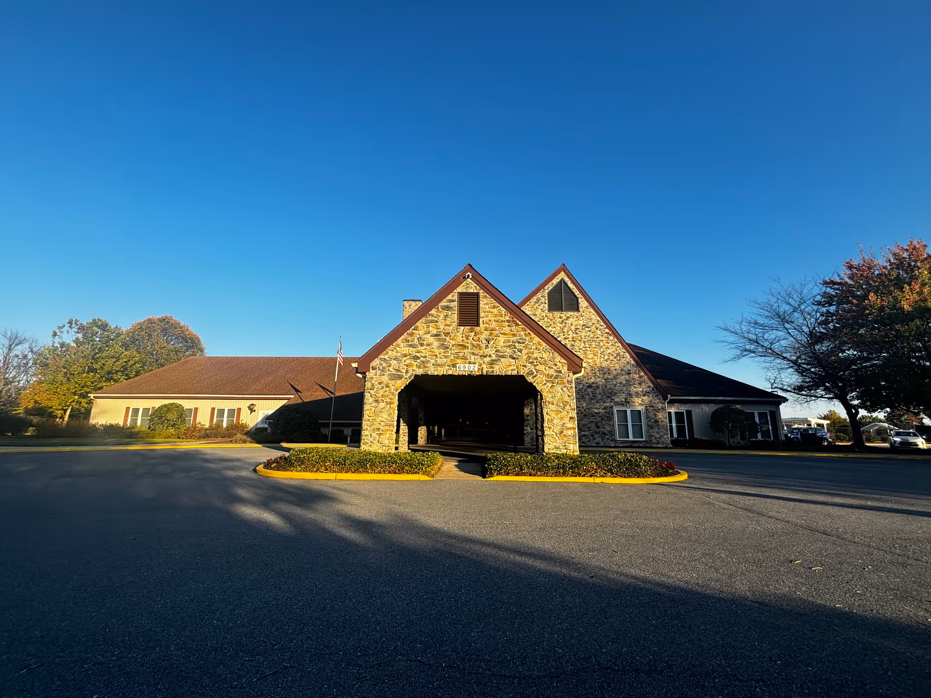 Front exterior view of a senior living facility building with a stone entrance and a driveway under a clear blue sky.