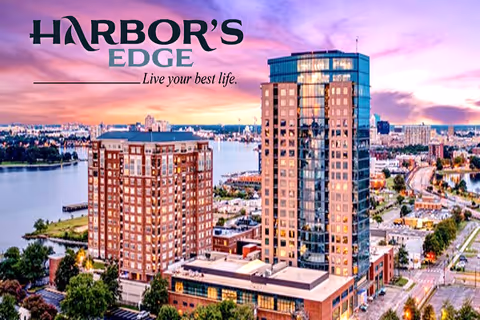 Aerial view of a waterfront urban area at sunset featuring two prominent multi-story buildings with a river and cityscape in the background. The image includes the text 'Harbor's Edge Live your best life.'