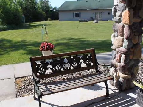 Outdoor bench beside a stone porch with a hanging planter and a neatly mown lawn