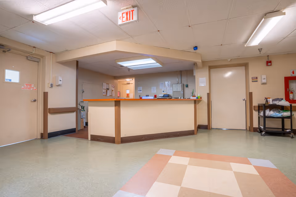 Empty nursing station reception area inside a clinical hallway with an EXIT sign overhead and a supply cart.