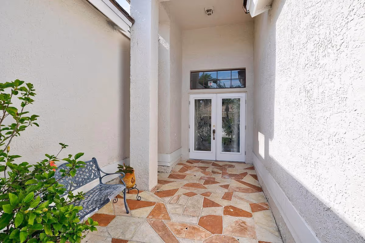 Covered entryway with double glass doors, patterned tile floor, a bench and potted plants.