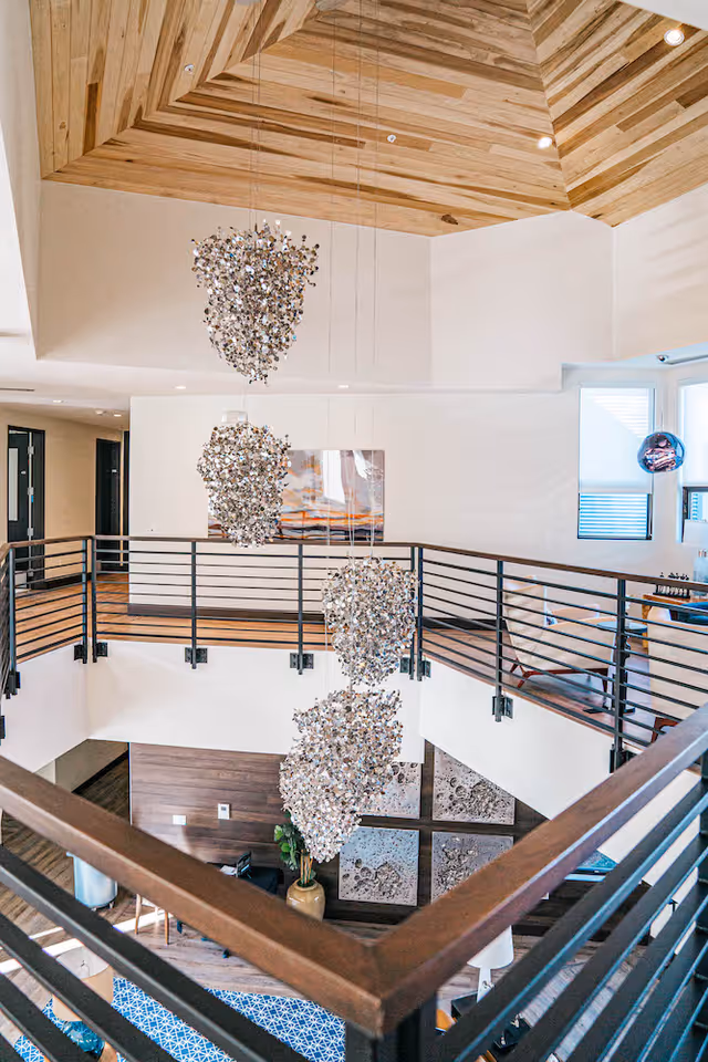 Multi-level atrium interior with clustered hanging chandeliers, metal railings, and a wooden ceiling.