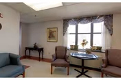 A small sitting area with upholstered chairs and a round table by a window with a floral valance and wall art.