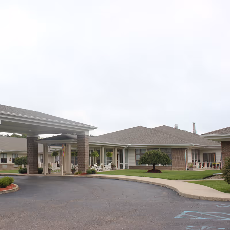 Covered entrance and driveway in front of a single-story senior care building with lawns and porches.
