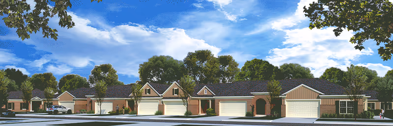 Exterior view of a senior living facility showing a row of single-story residential buildings with garages, surrounded by trees and under a partly cloudy blue sky.