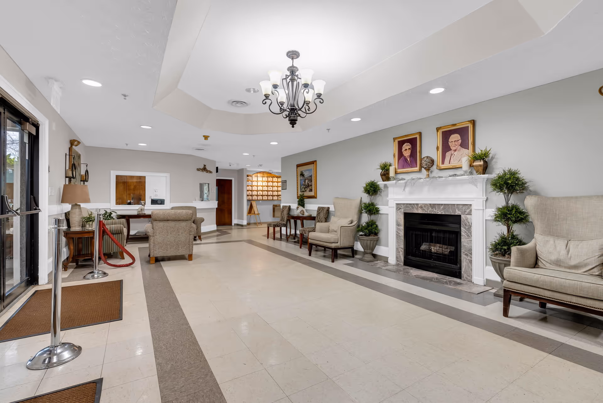 Spacious lobby area with armchairs arranged around a fireplace, a reception desk, and a chandelier overhead.