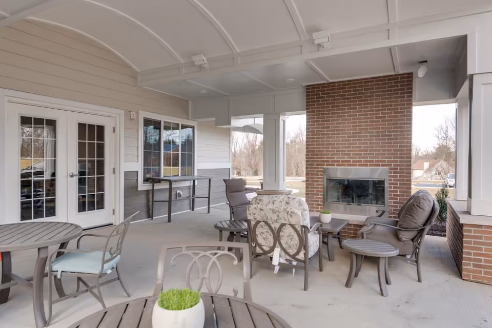 Covered outdoor patio with seating, tables, and a brick fireplace under an arched ceiling.