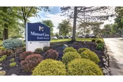 Outdoor view of a landscaped area with bushes and trees surrounding a sign that reads 'ManorCare Health Services' with a clear sky in the background.