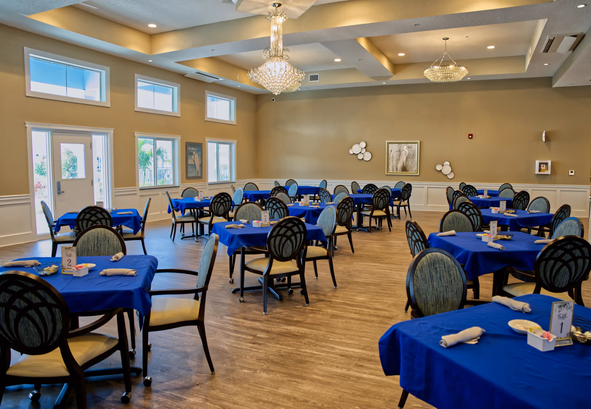 Elegant dining hall with blue tablecloths, many chairs, and crystal chandeliers.