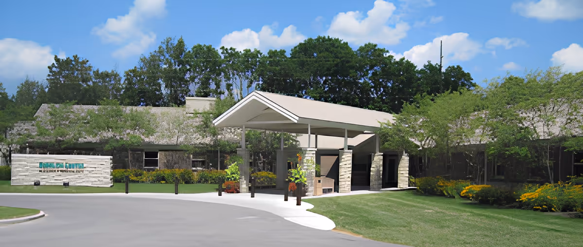 Exterior front entrance of a single-story memory care center with a covered porte-cochère, landscaped lawn, and signage.