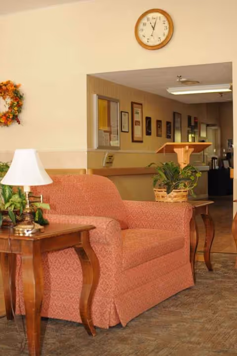 Indoor lounge at a senior living center with coral sofa, plants, and a wall clock.