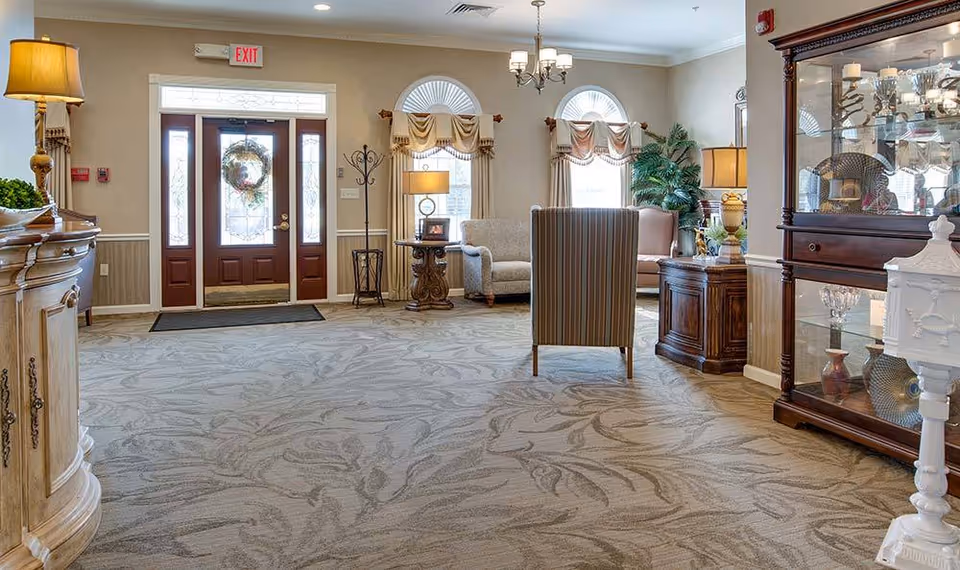 Carpeted senior living facility lobby with seating, decorative furniture, and a glass-paned front door.