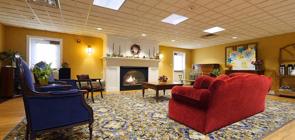 Community lounge with a lit fireplace, a red sofa, blue armchairs, a patterned rug, and additional seating and decor.