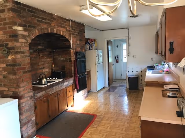 Long kitchen with a brick cooking alcove and built-in stove, refrigerator, countertops, and wooden cabinets.