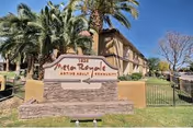 Entrance sign reading "Mesa Royale Active Adult Community" in front of a tan apartment building with palm trees under a clear blue sky.