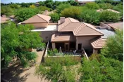 Aerial view of a single-story southwestern-style building with tan tiled roofs, a small enclosed patio, and surrounding desert landscaping.