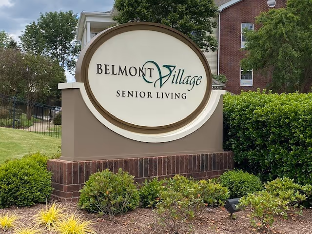 Front exterior sign reads Belmont Village Senior Living Memphis, surrounded by trimmed bushes.