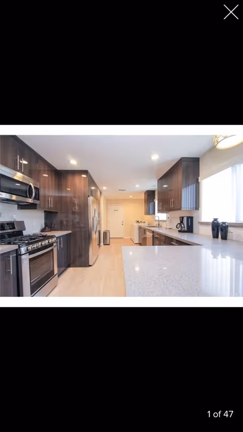 Modern kitchen with stainless steel appliances, dark wood cabinets, and a large light-colored island countertop.