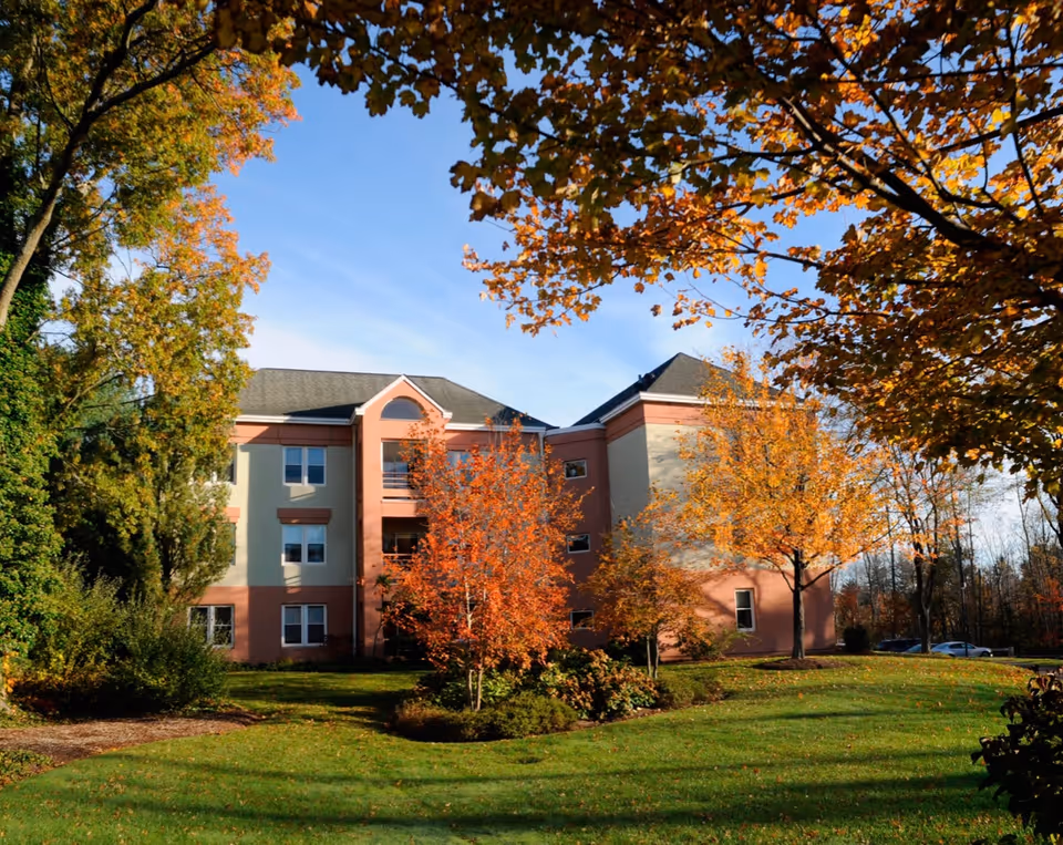 Exterior view of a multi-story residential building surrounded by green lawn and trees with autumn foliage under a clear blue sky.