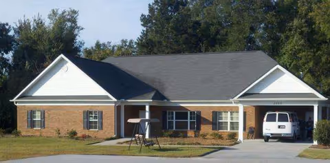 Exterior view of a single-story brick senior living facility with a driveway and van.