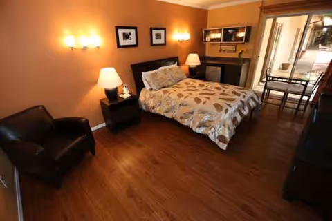 A warmly lit senior living bedroom with a bed, nightstands, lamps, and seating area.