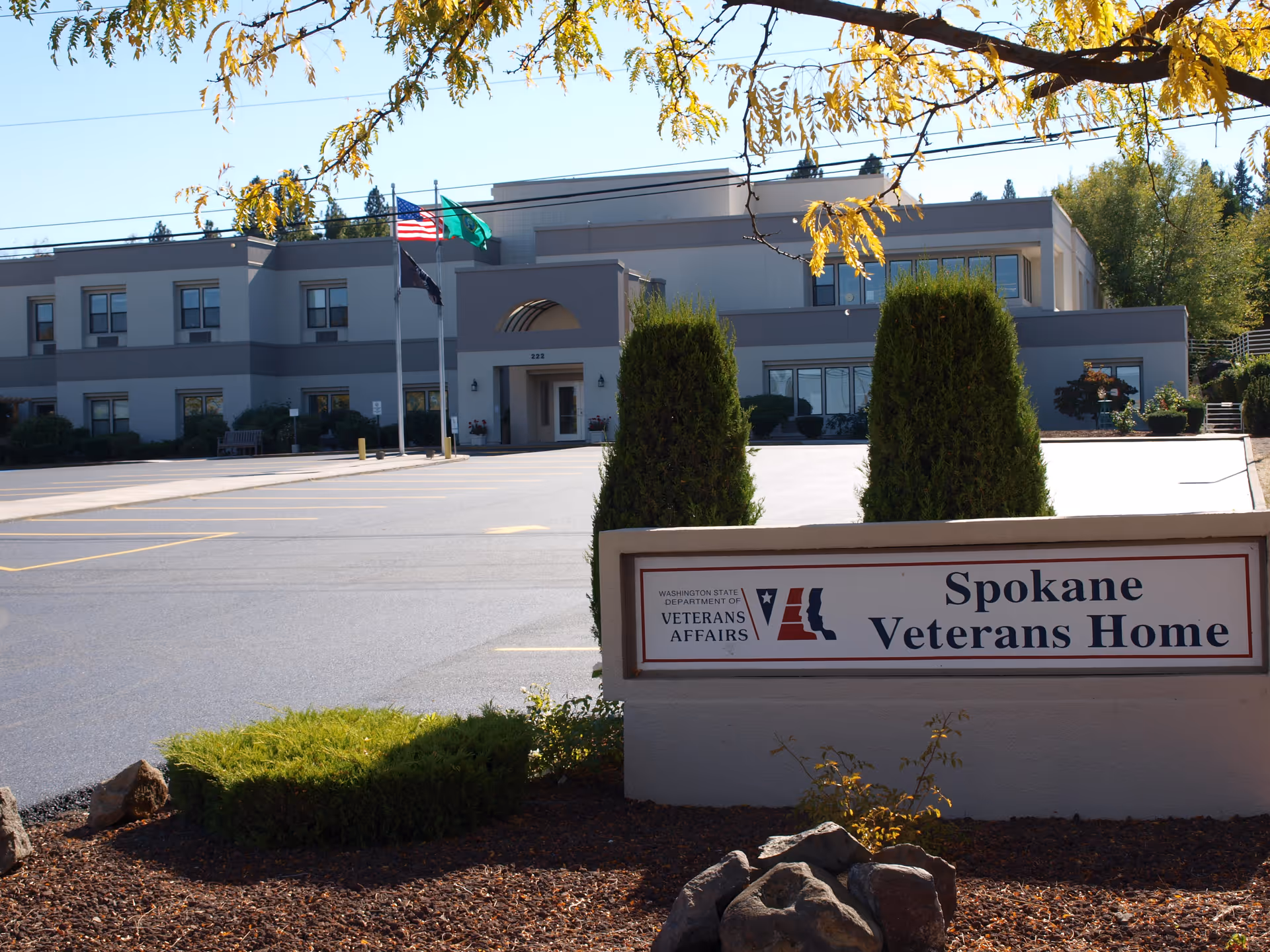 Exterior view of the Spokane Veterans Home building with a sign, two flagpoles, and landscaping in front.