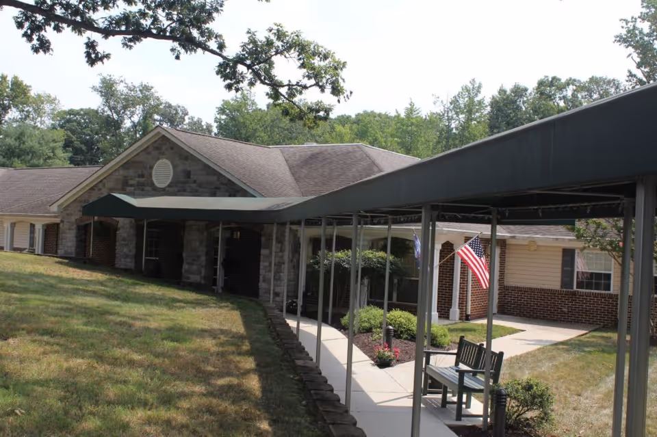 Covered walkway leading to the entrance of a single-story brick and stone senior living building with an American flag.