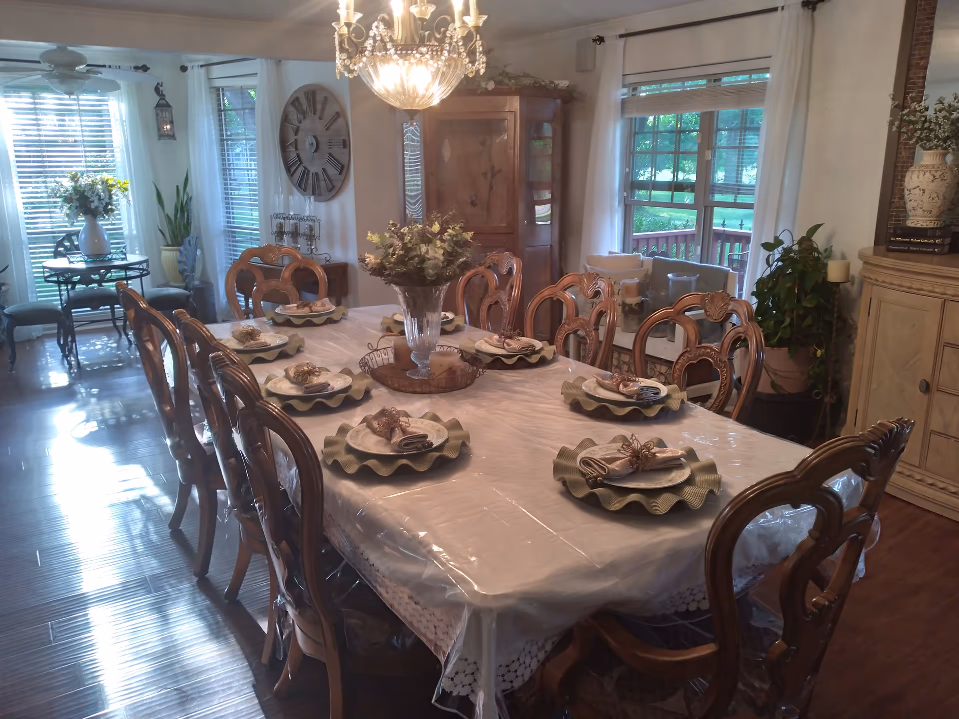 Formal dining room with a long set table, ornate wooden chairs, a chandelier and large windows.