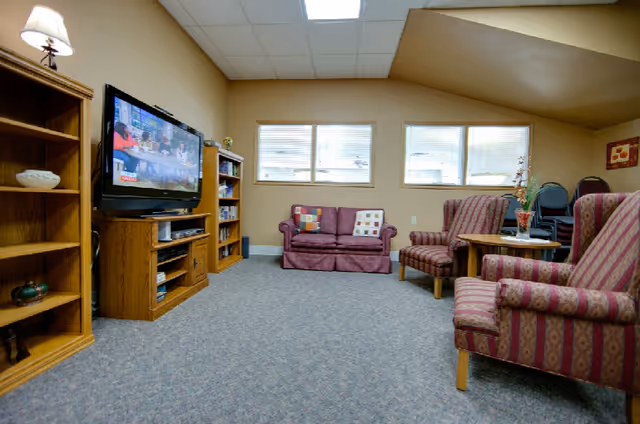 Cozy lounge with a TV, bookshelves, a sofa and several upholstered armchairs in a communal room.
